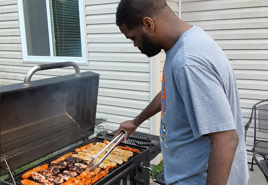 Resident cooks kabobs on an outdoor grill.