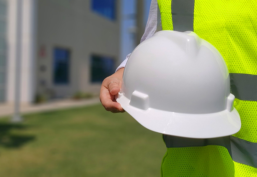 Person wears a safety vest and holds a hard hat