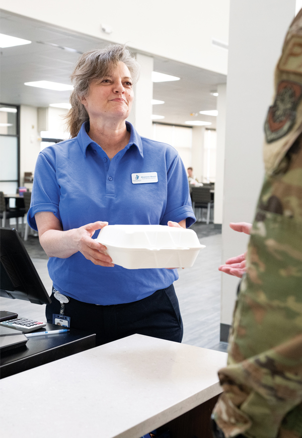 Woman cashier hands to-go container to man at checkout.