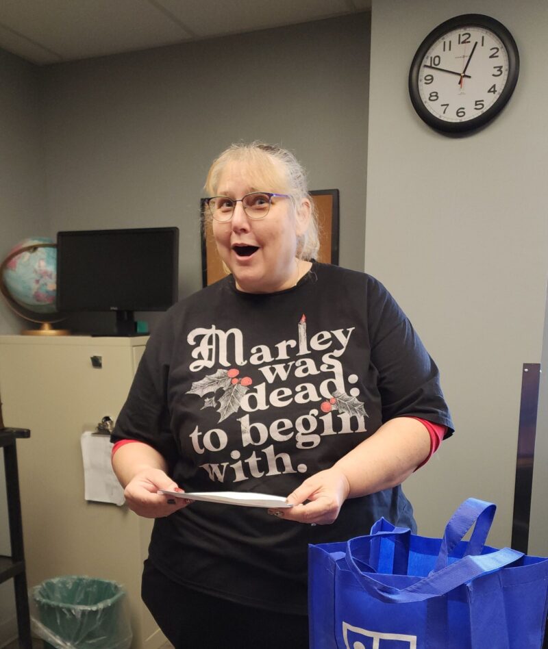 Janet Gentry excitedly holding a check while standing in an office, showing joy and surprise.