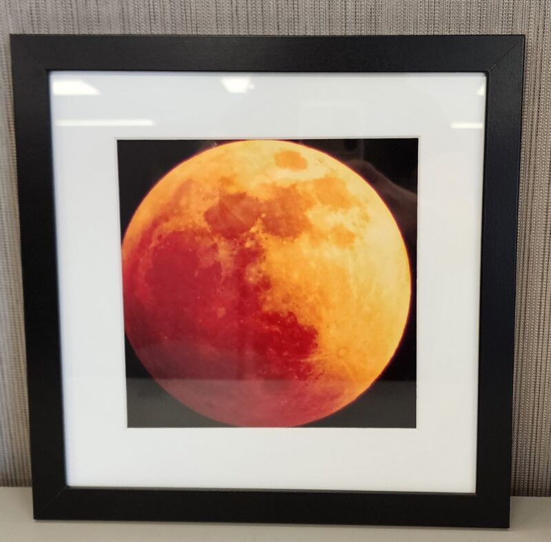 A framed photograph of a vibrant red and orange blood moon against a black background.