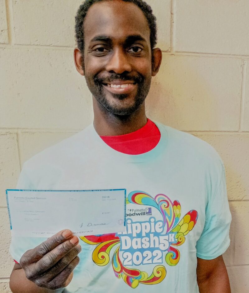 Montrell Graham proudly holding a check and smiling while wearing a "Hippie Dash 5K 2022" t-shirt.